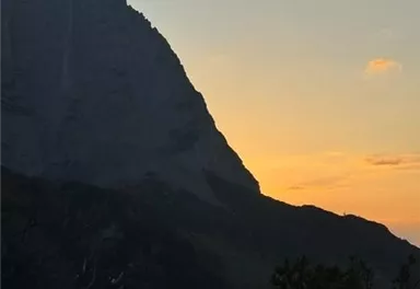 Ein majestätischer Berg im Hintergrund mit einem orangefarbenen Sonnenuntergang. Die Silhouette des Berges hebt sich gegen den Himmel ab.