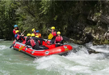 Eine Gruppe von Menschen fährt in einem roten Schlauchboot auf einem wilden Fluss. Sie tragen Helme und schwimmen in einer aufregenden Umgebung.
