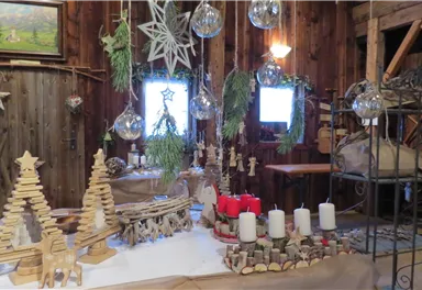 Eine gemütliche Weihnachtsdekoration mit Holzfiguren und Kerzen. Im Hintergrund sind rustikale Wände und festliche Elemente zu sehen.