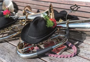 Eine Ansammlung von Blasinstrumenten auf einer Holzoberfläche. Einige Instrumente tragen schwarze Hüte mit Blumen und Dekoration.