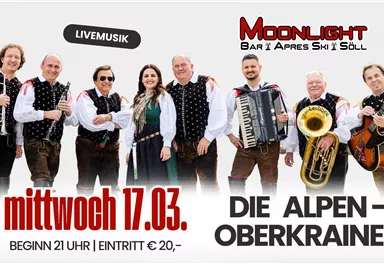 Eine Gruppe von Musikern steht zusammen und lächelt in traditioneller Kleidung. Im Hintergrund steht der Schriftzug „Moonlight Bar Après Ski Söll“ zur Feier des 25-jährigen Bestehens.