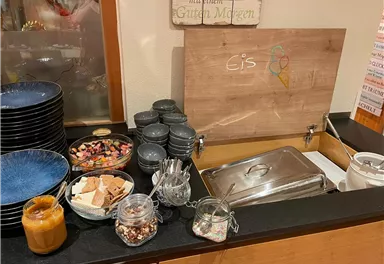 Ein freistehender Eisbuffet mit verschiedenen Toppings und Schalen. Die Präsentation beinhaltet auch Gläser mit süßen Leckereien und Schüsseln zum Servieren.
