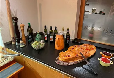 Ein gedeckter Tisch mit verschiedenen Ölen, einem Salat und einem großen Stück Kuchen. Dazu stehen Gewürzmühlen und eine dekorative Karaffe.