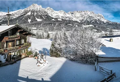 Eine malerische Winterlandschaft mit schneebedeckten Bergen und einem traditionellen Chalet. Der klare Himmel verleiht der Szene eine ruhige Atmosphäre.