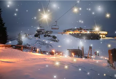 Ein verschneites Berggebiet bei Nacht mit einem Skilift und einem Gebäude im Hintergrund. Der Himmel ist mit funkelnden Elementen verziert, die eine magische Atmosphäre erzeugen.