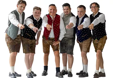 Sechs Männer in traditioneller bayerischer Tracht stehen nebeneinander und zeigen mit dem Finger nach vorn. Sie tragen Lederhosen und farbige Westen, die festlich und einladend wirken.