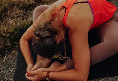 Eine Person macht eine Yoga-Übung auf einer Matte im Freien. Sie beugt sich vor und hält einen Fuß.