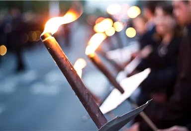 A group of people holds torches in the twilight. The flames shine in the darkness, creating a festive atmosphere.