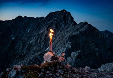 A torch burns on a rock in the mountains. In the background, impressive mountain peaks and a dark sky can be seen.