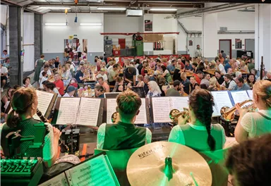 A large event with many people sitting at tables. In the foreground, musicians are playing in traditional clothing.