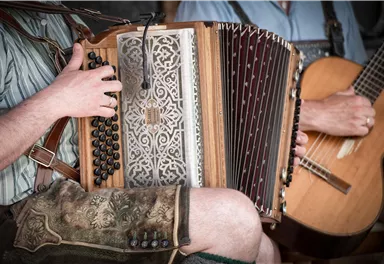 Ein Musiker spielt auf einem Akkordeon, während ein anderer Musiker eine Gitarre hält. Beide tragen traditionelle Kleidung.