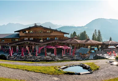 A picturesque Alpine house with an inviting terrace and a view of the mountains. The surroundings are green and sunny, ideal for a relaxing stay.