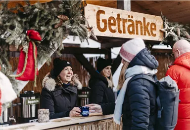 Ein Getränkestand mit festlicher Dekoration. Eine Verkäuferin lächelt, während Kunden Getränke bestellen.