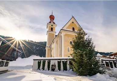 Eine schöne Kirche in einer schneebedeckten Landschaft. Die Sonne scheint hinter den Bergen und beleuchtet die Umgebung.