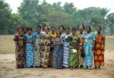 Eine Gruppe von Frauen in bunten traditionellen Kleidern steht in einem Park. Im Hintergrund sind Bäume und eine grüne Landschaft zu sehen.