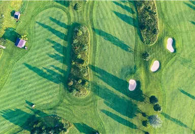 A stylish golf course with well-maintained greens and sand bunkers. Long shadows fall from the trees onto the fairway.