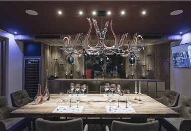 Ein eleganter Essbereich mit einem großen Holztisch und stilvollen Stühlen. Über dem Tisch hängt eine auffällige Lampe, umgeben von dekorativen Elementen.