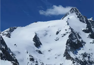 Ein majestätischer Berg mit schneebedeckten Gipfeln unter einem klaren blauen Himmel. Die Landschaft strahlt Kälte und Schönheit aus.