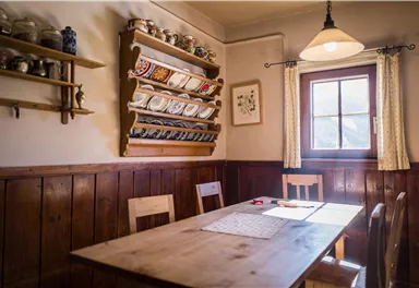 A cozy dining area with a wooden table and chairs. Dishes and decorations are hanging on the wall.