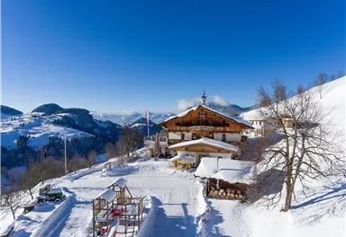 Ein malerisches Bergdorf im Schnee mit einer gemütlichen Hütte. Der Himmel ist klar und blau, umgeben von schneebedeckten Hügeln.
