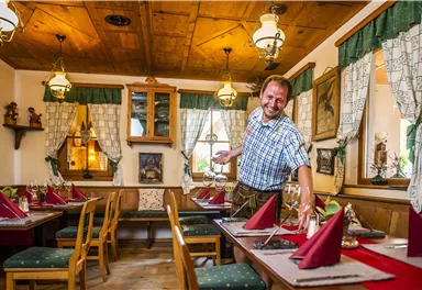 Ein gemütliches Restaurant mit Holzdekor und traditioneller Einrichtung. Ein lächelnder Kellner deckt den Tisch für die Gäste.