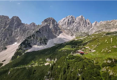 Eine beeindruckende Berglandschaft mit hohen Felsen und grünen Wiesen. Im Vordergrund befindet sich ein rotes Haus in der idyllischen Natur.