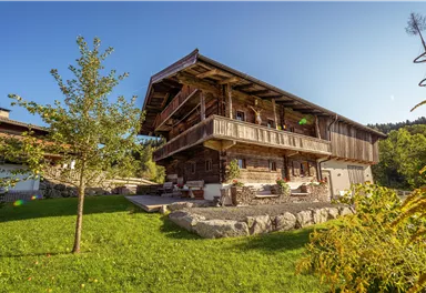 Ein gemütliches Holzhaus mit mehreren Balkonen und einem großen Garten. Die Sonne scheint und der Himmel ist klar.