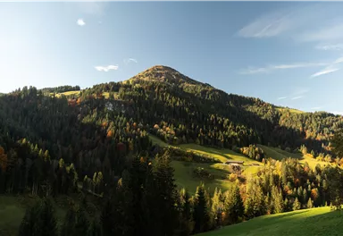 Zwei Radfahrer stehen auf einer Wiese und blicken auf eine wunderschöne Berglandschaft. Die Sonne geht gerade unter und schafft eine malerische Atmosphäre.