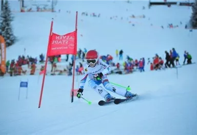 Ein Skifahrer fährt durch ein Tor auf einer verschneiten Piste. Im Hintergrund sind viele Zuschauer und weitere Skifahrer zu sehen.