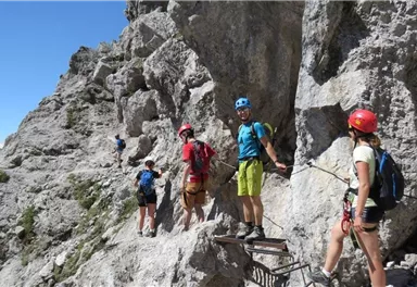 Gruppe von Kletterern auf einem felsigen Weg in den Bergen. Sie tragen Helme und Kletterausrüstung.