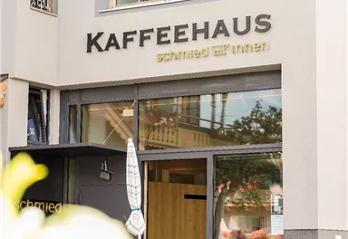 Ein gemütliches Kaffeehaus mit einer einladenden Fassade. Im Inneren sitzen Gäste und genießen ihre Getränke.