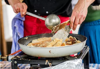 A person is cooking in a pan on a gas stove. You can see them flipping the food with a spatula.