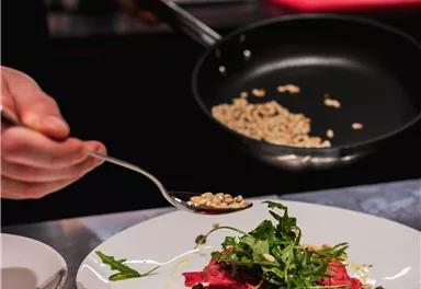 A chef places fine ingredients on an elegant dish. In the foreground, you can see a plate with raw meat and fresh vegetables.