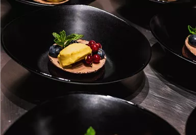 An elegant dessert presentation in black bowls. The desserts are decorated with berries and a yellow sorbet ball.