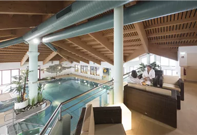 Ein moderner Wellnessbereich mit einem großen Pool und gemütlichen Sitzgelegenheiten. Pflanzen und Holzdetails schaffen eine entspannte Atmosphäre.
