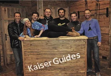Eine Gruppe von sieben Personen steht lächelnd an einer Holztheke. Die Umgebung hat einen rustikalen, gemütlichen Charme.