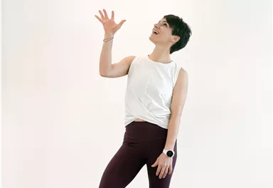 A person is standing on a yoga mat and juggling a ball. They are wearing sporty attire and smiling.