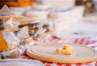 A selection of packaged cheese on a table with a wooden board in the foreground. Some cheese cubes are on the board.