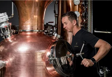A man is working on a copper distillation plant. Pressure gauges are visible in the background.