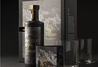 An elegant gift set consisting of a bottle of spirits, two glasses, and a companion book. The packaging is simple and modern, featuring a mountain motif and golden lettering.