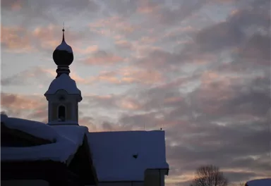Eine sanfte Silhouette eines Gebäudes mit einem kuppelähnlichen Turm, umgeben von Schnee. Der Himmel zeigt ein Farbenspiel aus Rosa und Grau in der Dämmerung.