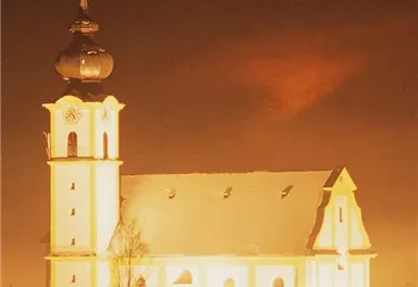 Eine wunderschöne Kirche im verschneiten Dorf bei Nacht. Der Turm leuchtet hell und schafft eine festliche Atmosphäre.