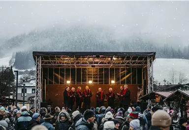 A festive event with a stage where singers in red vests perform. Many people stand in front of it and enjoy the atmosphere in a wintry setting.