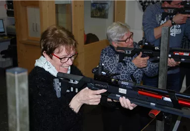 Two women are standing at a shooting range and aiming with air rifles. Both have concentrated expressions and are wearing goggles.