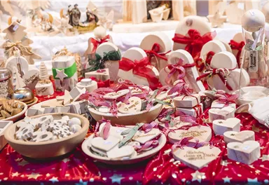 Ein festlicher Tisch mit handgemachten Geschenken und Dekorationen. Die Objekte sind in verschiedenen Formen und Farben, umgeben von rotem Tuch mit Sternen.