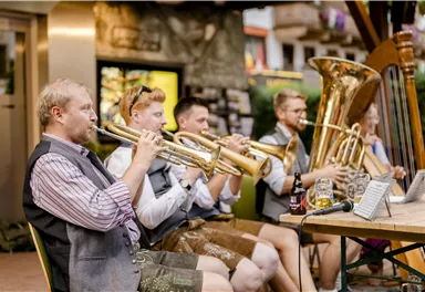 Eine Gruppe von vier Musikern spielt traditionelle Musik in einem malerischen Innenhof. Zu sehen sind eine Harfe, ein Kontrabass und zwei Akkordeons.