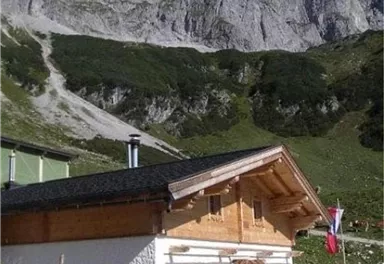 A cozy wooden house in the mountains, surrounded by majestic rocks. In the background, green meadows and a clear blue sky can be seen.