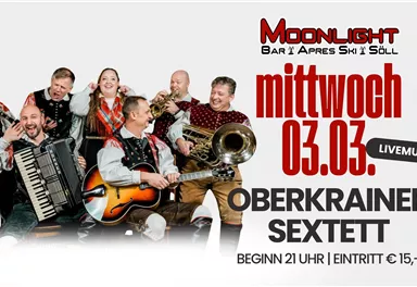 Eine Musikkapelle, bestehend aus sieben Personen, steht zusammen und lächelt. Sie tragen traditionelle Kleidung und halten verschiedene Musikinstrumente in den Händen.