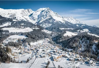 Ein malerisches Bergdorf im Winter, umgeben von schneebedeckten Gipfeln. Die Landschaft ist ruhig und idyllisch, mit vielen traditionellen Häusern.