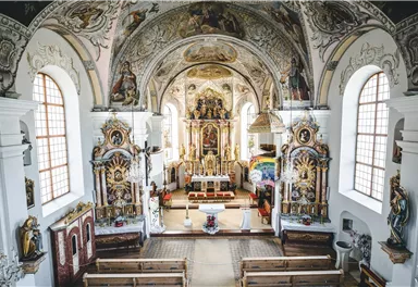 A magnificent church with a high vaulted ceiling and ornate frescoes. In the altar area, stylish furniture is present, and the atmosphere feels solemn.